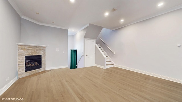 unfurnished living room with wood finished floors, a fireplace, crown molding, baseboards, and stairs