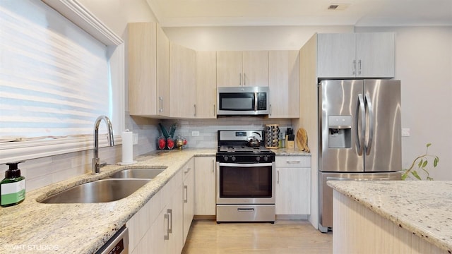 kitchen featuring tasteful backsplash, appliances with stainless steel finishes, light stone counters, and a sink