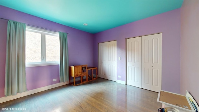 unfurnished bedroom featuring baseboards, two closets, and wood finished floors