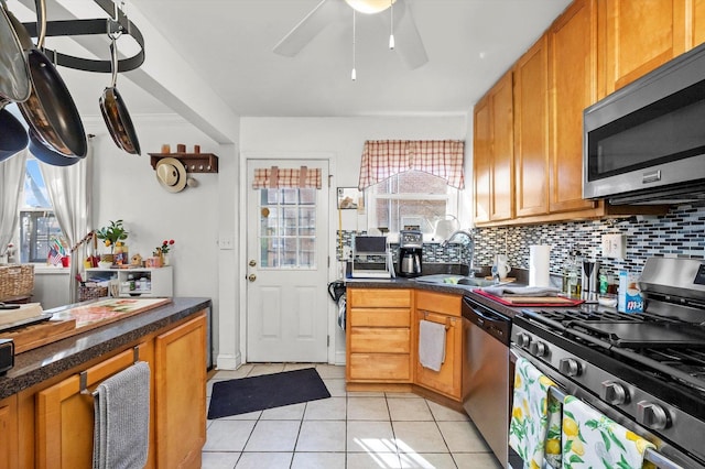 kitchen with light tile patterned floors, a sink, appliances with stainless steel finishes, tasteful backsplash, and dark countertops