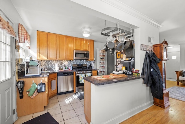 kitchen featuring stainless steel appliances, a peninsula, backsplash, dark countertops, and crown molding