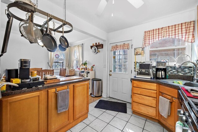 kitchen featuring tasteful backsplash, brown cabinetry, light tile patterned flooring, a sink, and ceiling fan