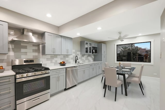 kitchen featuring wall chimney range hood, gray cabinets, marble finish floor, and stainless steel appliances