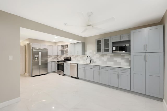 kitchen featuring stainless steel appliances, gray cabinetry, decorative backsplash, a sink, and wall chimney exhaust hood