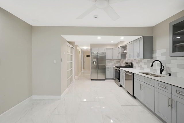 kitchen featuring stainless steel appliances, decorative backsplash, gray cabinetry, a sink, and wall chimney range hood