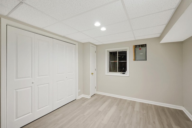 unfurnished bedroom featuring a drop ceiling, baseboards, a closet, electric panel, and light wood finished floors