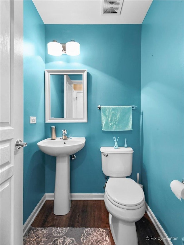 half bathroom featuring wood finished floors, visible vents, and baseboards