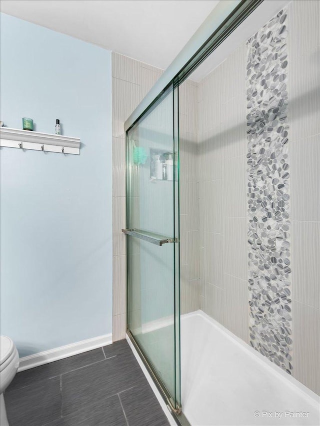 bathroom with a shower stall, toilet, and baseboards