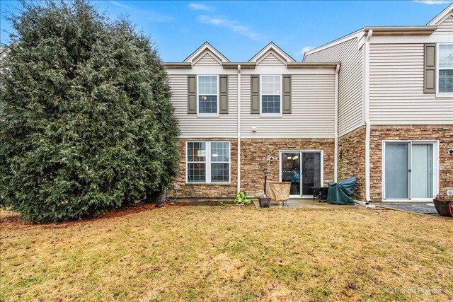 rear view of property featuring stone siding, a patio area, and a lawn