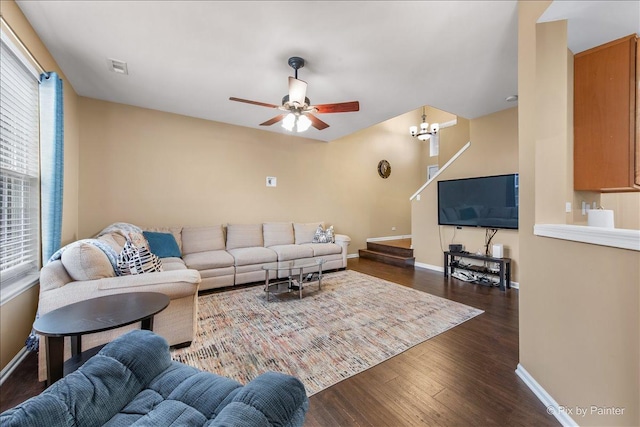 living area featuring dark wood-style floors, ceiling fan with notable chandelier, and baseboards