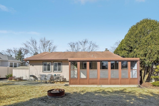 rear view of property with a patio, an outdoor fire pit, a sunroom, a chimney, and a lawn