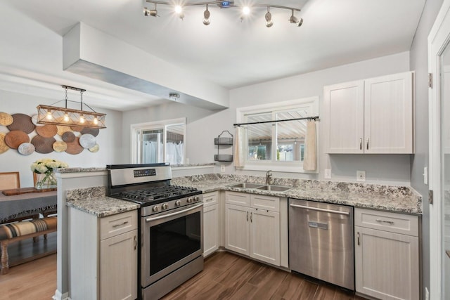 kitchen featuring light stone countertops, a peninsula, dark wood-style floors, stainless steel appliances, and a sink