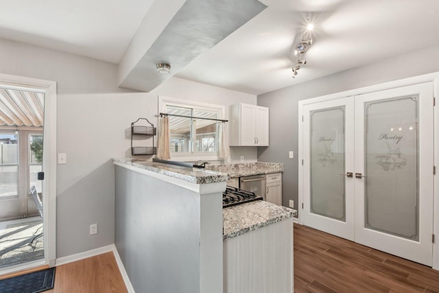 kitchen featuring baseboards, french doors, wood finished floors, white cabinetry, and stainless steel dishwasher