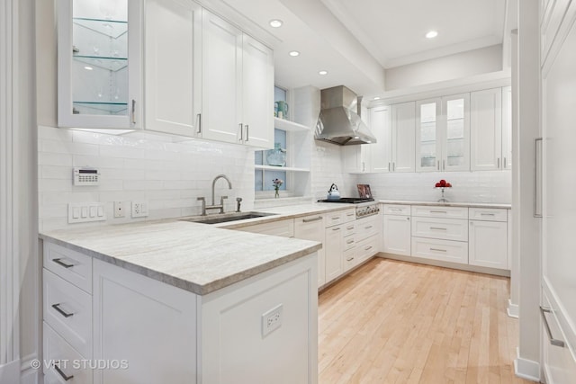 kitchen with a sink, white cabinetry, wall chimney range hood, and open shelves