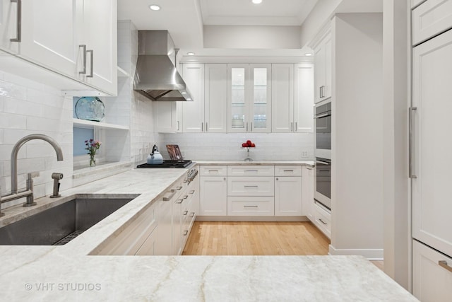 kitchen featuring gas stovetop, a sink, light stone counters, white cabinets, and wall chimney exhaust hood
