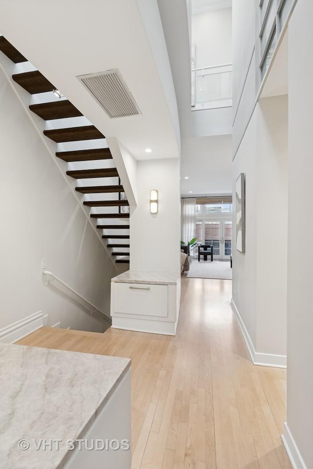 entrance foyer with stairway, baseboards, a high ceiling, light wood-style floors, and visible vents