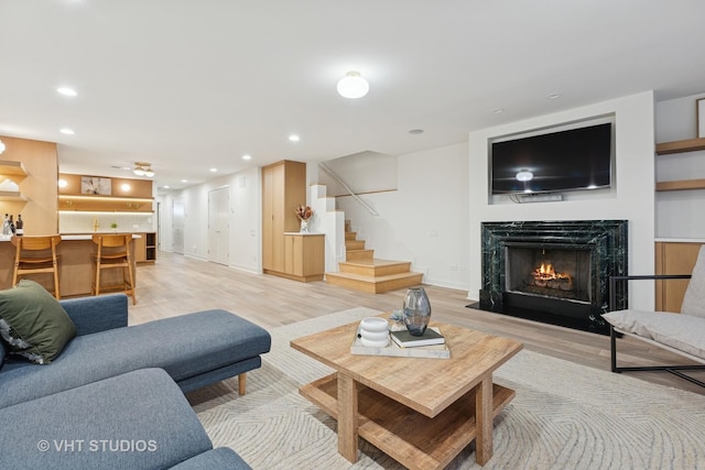 living area with a high end fireplace, light wood-style flooring, stairway, and recessed lighting