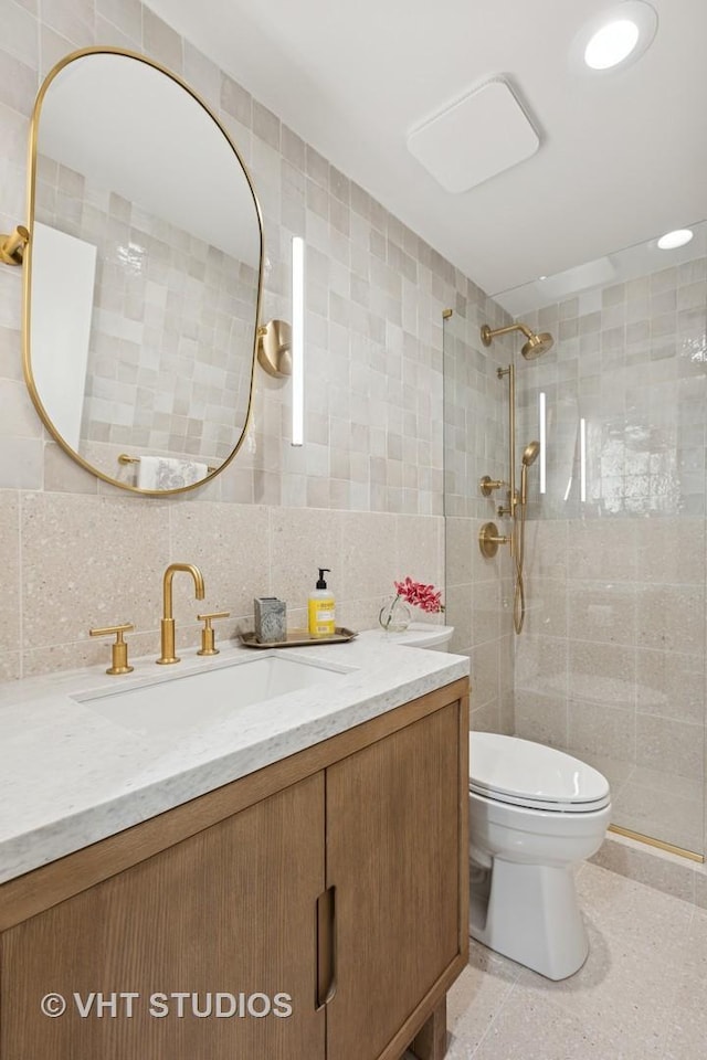 full bath featuring a tile shower, toilet, vanity, and tile walls
