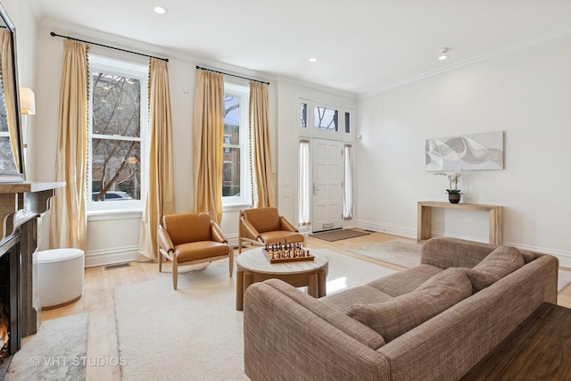 living area featuring ornamental molding, baseboards, a lit fireplace, visible vents, and light wood-style flooring