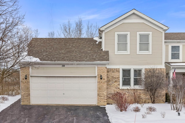 traditional-style house with a garage, driveway, a shingled roof, and brick siding