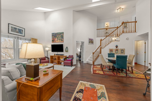 living room with dark wood-type flooring, a towering ceiling, an inviting chandelier, and stairs