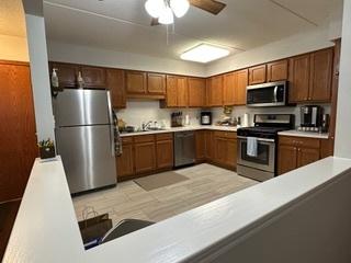 kitchen with brown cabinets, stainless steel appliances, light countertops, and a ceiling fan