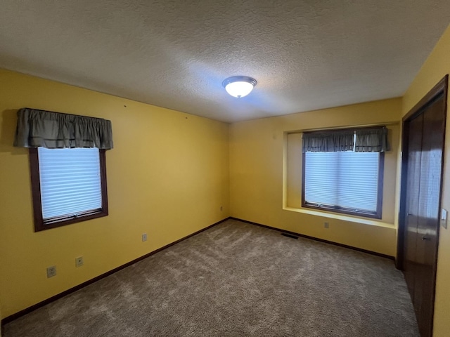 carpeted spare room with visible vents, a textured ceiling, and baseboards