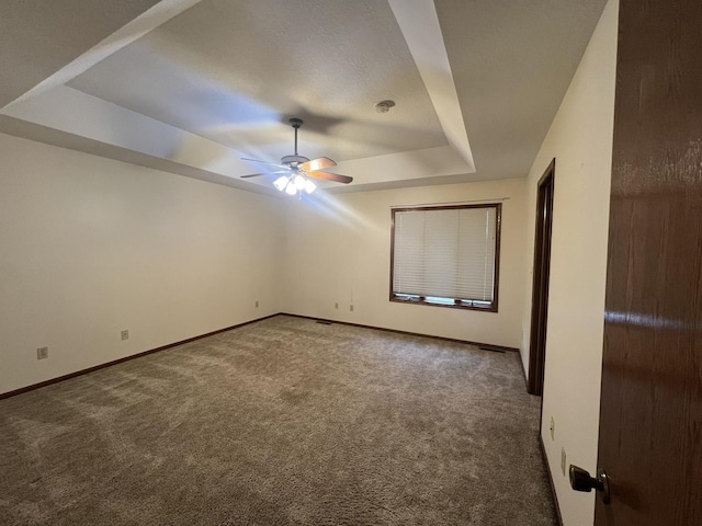 carpeted empty room with ceiling fan, baseboards, and a raised ceiling