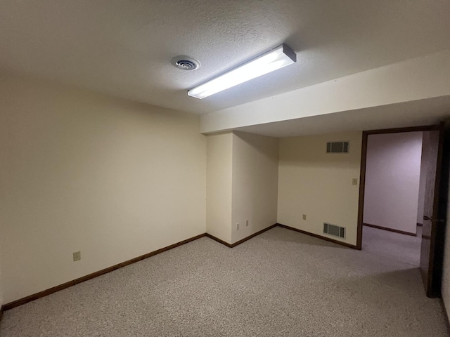 finished below grade area with light carpet, visible vents, and a textured ceiling