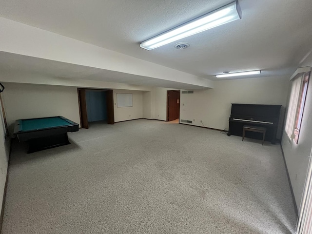 finished basement with light colored carpet, visible vents, billiards, and a textured ceiling