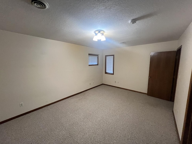 spare room featuring light colored carpet, visible vents, a textured ceiling, and baseboards