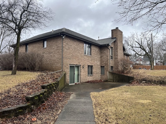 rear view of property featuring a yard, brick siding, a chimney, and fence