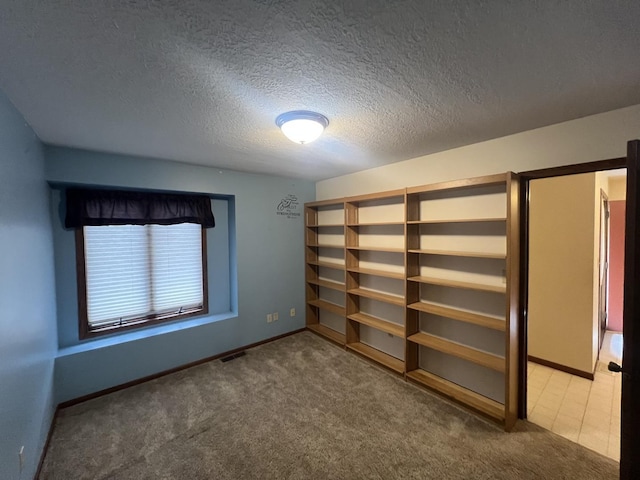 empty room with carpet, visible vents, a textured ceiling, and baseboards