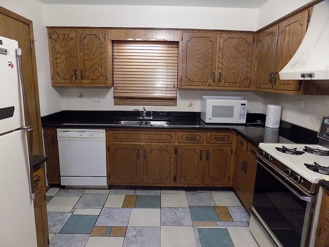 kitchen featuring white appliances, dark countertops, a sink, and under cabinet range hood