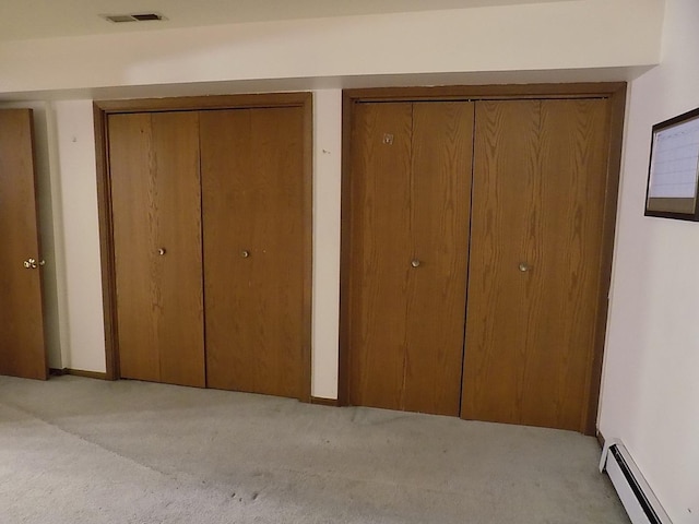 unfurnished bedroom with a baseboard heating unit, light colored carpet, visible vents, and two closets