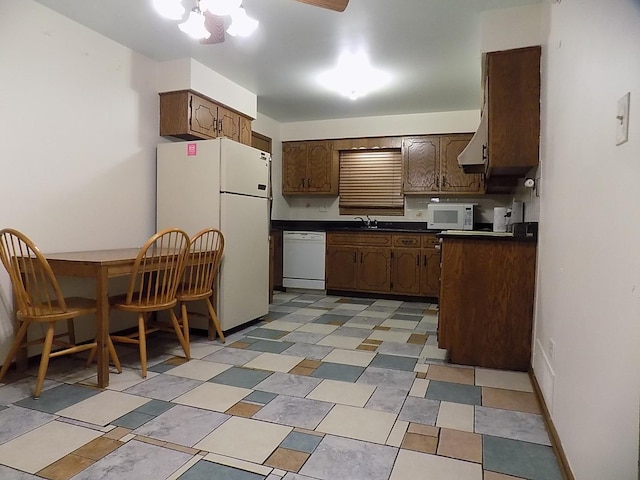 kitchen featuring dark countertops, white appliances, light floors, and a sink