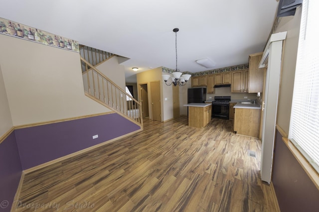 kitchen featuring wood finished floors, a kitchen island, black appliances, light countertops, and a notable chandelier