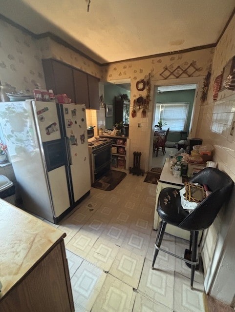 kitchen with wallpapered walls, crown molding, white refrigerator with ice dispenser, and light floors