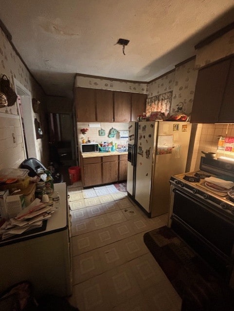 kitchen with white refrigerator with ice dispenser, light floors, a textured ceiling, gas range, and wallpapered walls