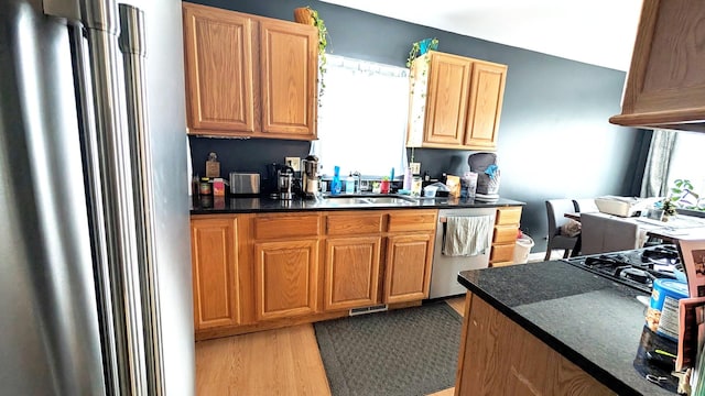 kitchen with stainless steel appliances, dark countertops, a sink, and light wood-style flooring