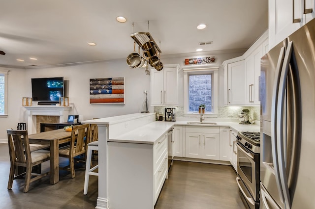 kitchen featuring a sink, white cabinetry, appliances with stainless steel finishes, a peninsula, and decorative backsplash