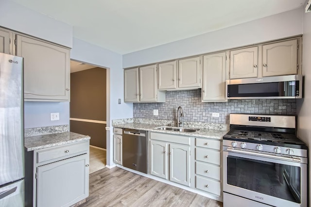 kitchen featuring stainless steel appliances, decorative backsplash, light wood-style floors, a sink, and light stone countertops