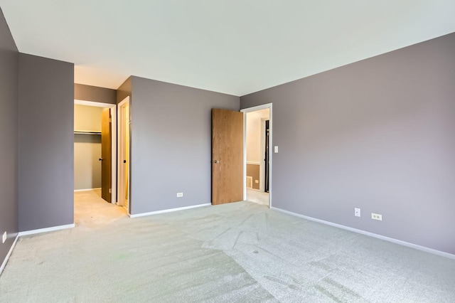 unfurnished bedroom with baseboards, a walk in closet, and light colored carpet