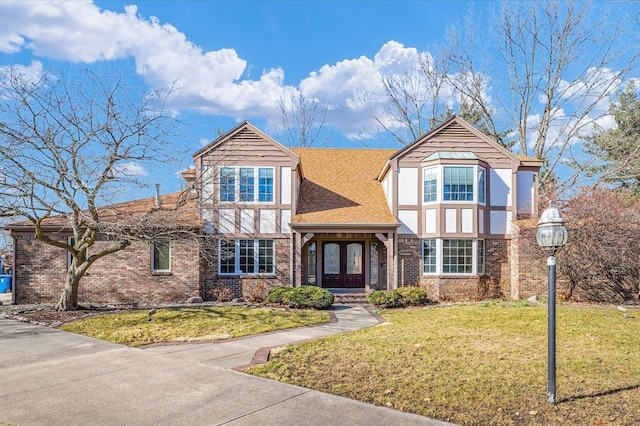 english style home with brick siding, a front lawn, and roof with shingles