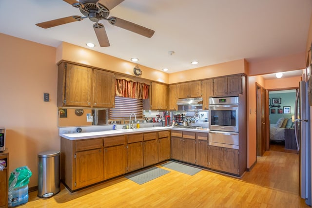 kitchen featuring a warming drawer, light countertops, appliances with stainless steel finishes, a sink, and under cabinet range hood