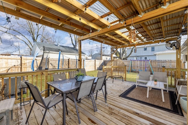 wooden deck featuring a fenced backyard, a trampoline, outdoor dining space, and a lawn