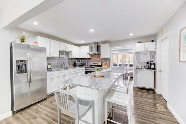 kitchen featuring white cabinetry, stainless steel appliances, wall chimney exhaust hood, and a sink