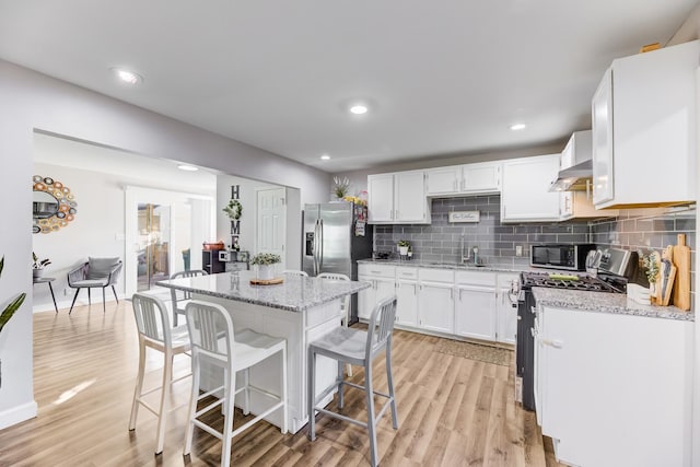 kitchen featuring light wood-type flooring, light stone counters, backsplash, stainless steel appliances, and white cabinets