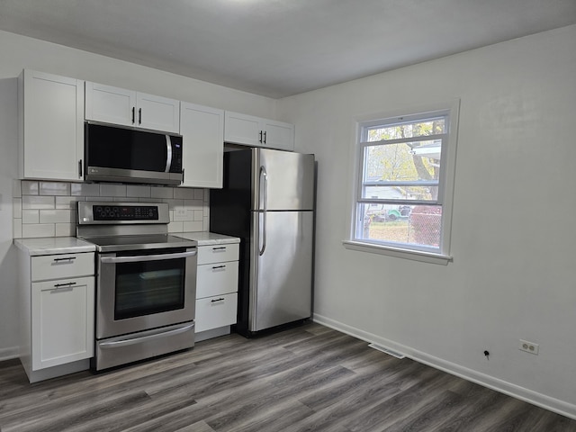 kitchen with dark wood-type flooring, white cabinets, light countertops, appliances with stainless steel finishes, and decorative backsplash