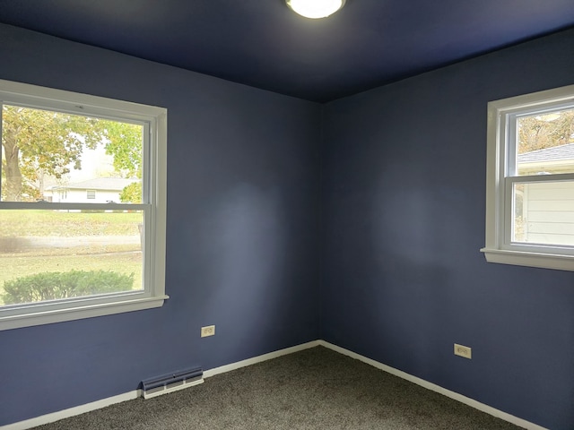 unfurnished room with plenty of natural light, dark carpet, visible vents, and baseboards